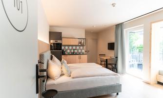 A modern room with two beds and a small kitchenette.  
Large windows allow for plenty of natural light and access to the terrace.