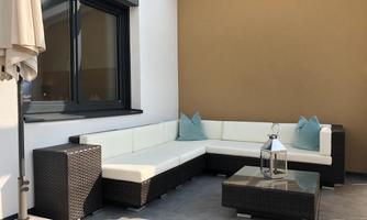 A stylish outdoor area with a modern corner sofa and cushions in soft colors. An elegant table and a sun umbrella complete the relaxed atmosphere.