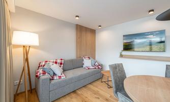 A modern living room setup with a gray sofa, a round dining table, and a cozy floor lamp. The walls are light and a picture of a landscape adorns the wall.