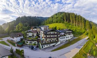 A picturesque landscape with hills, trees, and a charming building by the roadside. The sky is clear and slightly cloudy, creating a calm atmosphere.