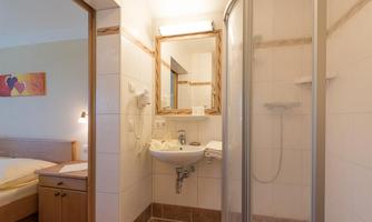 A modern bathroom with a shower, a sink, and a large mirror. The walls are brightly tiled and the room design is simple and functional.