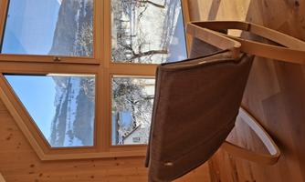 A cozy armchair sits in front of a large window overlooking snow-covered mountains. The warm wooden walls create an inviting atmosphere.