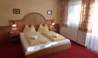 A cozy bedroom with a double bed and wooden paneling. The windows are decorated with curtains, and the carpet is red.