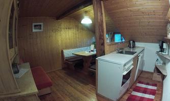 A cozy, rustic kitchen with wooden ceilings and walls. There is a seating area and a modern cooking panel.