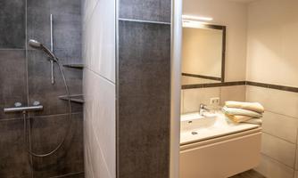 A modern bathroom with a shower and a bathtub. The walls are decorated with gray tiles, and fresh towels are ready.