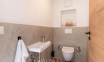 A modern bathroom with a stylish sink and a toilet. The walls are elegantly designed in neutral colors.