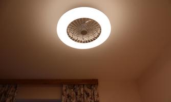 A modern ceiling light with a round design and bright light. The background features a bright wall and curtains.