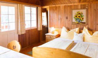A cozy bedroom with wooden paneling and two beds. Large windows bring a lot of daylight into the room.