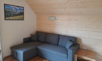 A cozy living room with a gray corner sofa and a small wooden table. A picture of a mountain landscape hangs on the wall.