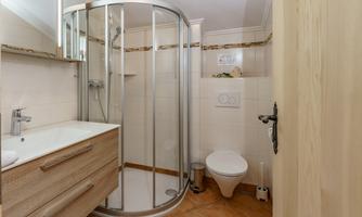 A modern bathroom with a shower cubicle and a sink. The walls are tiled in light colors, and the floor is made of terracotta-colored tiles.