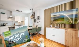 A modern living room with an open kitchen and cozy dining area. On the table lies a summer menu showcasing special offers.