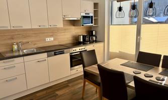 A modern kitchen with light cabinets and wooden surfaces. A dining table with dark chairs complements the space.