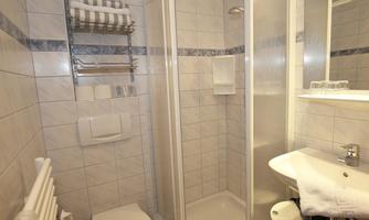 A modern bathroom with a shower, sink, and towel holders. The walls are tiled, and it is bright and clean.