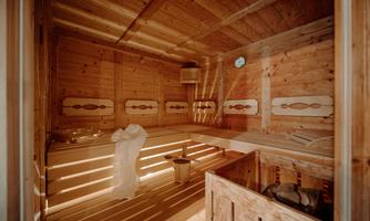 A cozy sauna with wooden paneling and soft lighting. Inside, there are benches and a bucket for water.