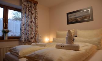 A cozy bedroom with two beds and soft pillows. The room is bright and cheerful, with a window and decorative curtain.