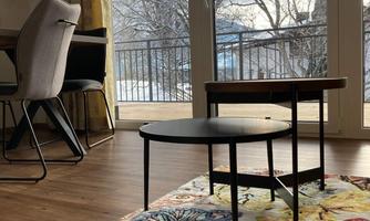 A cozy room with a colorful rug and a small table. Large windows provide a view of the outdoor area.