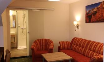 A cozy living room with a red sofa and two armchairs. In the background, a bathroom with a shower is visible.