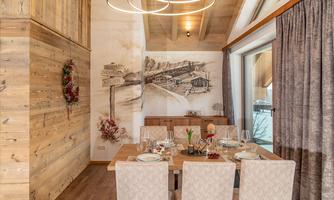 A stylish dining room with wooden paneling and a circular lamp. The table is beautifully set and a decorative mural adds charm to the space.