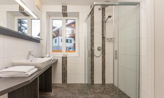 A modern bathroom with a shower and a sink. Large windows offer a view outside.
