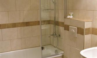 A modern bathroom with a bathtub and a glass shower. The walls are adorned with light tiles and a decorative brown line.