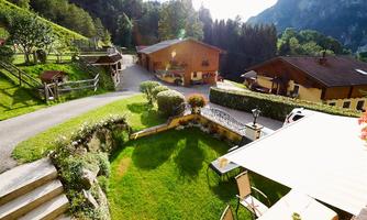 An idyllic landscape with a well-maintained garden and several wooden chalets. In the background, gentle hills and trees can be seen.