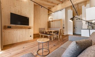 A modern living room with wood paneling and a large television. The room is bright and inviting, furnished with a dining table and comfortable furniture.