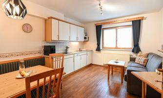 A bright kitchen with modern furniture and wooden flooring. A dining table and a cozy seating area provide space for relaxation.