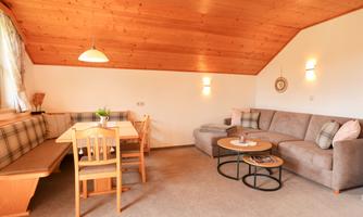 A cozy living space with wooden accents and plenty of natural light. The room is furnished with a seating area, a dining table, and a comfortable couch.