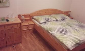 A cozy bedroom with a wooden bed and colorful bedding. Next to the bed is a small wooden wardrobe.