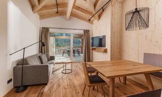 A modern living room with wood paneling and a large window that overlooks a terrace. The decor is cozy and in a minimalist style.