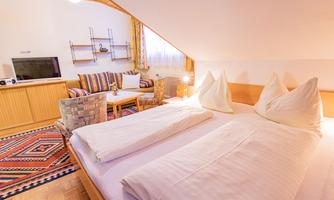 A cozy bedroom with two beds and pillows. In the background, there is a living area with a television and comfortable furniture.
