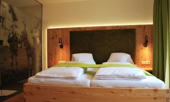 A modern bedroom with a double bed and cozy lighting. The walls are decorated with wood and a green headboard panel.