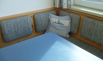 A cozy seating area with cushioned benches and a blue table. A pillow with a maritime pattern complements the decor.
