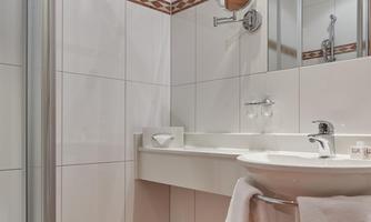 A modern bathroom with a shower, a sink, and a large mirror. The walls are adorned with white tiles and a decorative stripe.