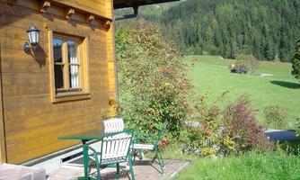 A cozy wooden cabin with a beautiful garden. In the background, green meadows and trees are visible.