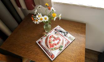 A wooden table with a vase of daisies. On it lies a magazine with a recipe for a heart cake and a pair of glasses.