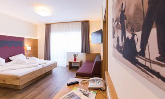 A modern hotel room with a cozy bed and a seating area. Large windows provide plenty of daylight and a view outside.