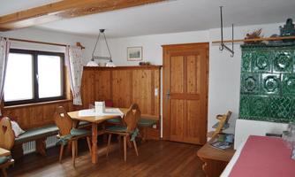 A cozy room with wooden furniture and a round table. On the wall, there is a decorated green tiled stove.