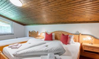A cozy bedroom with wooden walls and a large double bed. Decorative pillows and towels are placed on the bed.
