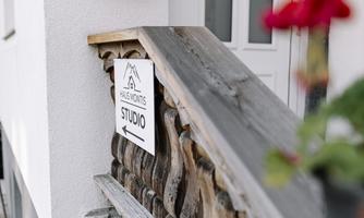 An inviting entrance to a studio with a wooden railing. On the left is a mailbox and a plant with red flowers.