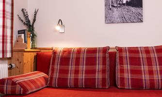 A cozy couch with red cushions in a checkered pattern. In the background, there is a picture on the wall and a green plant visible.