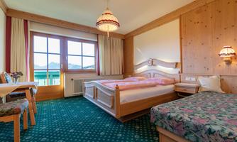 A cozy hotel room with a double bed and a single bed. Large windows offer a view of the mountains and let in plenty of daylight.