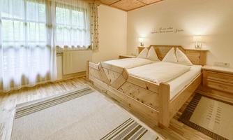 A cozy bedroom with two wooden single beds. The room has large windows that let in plenty of light and is furnished in a minimalist style.