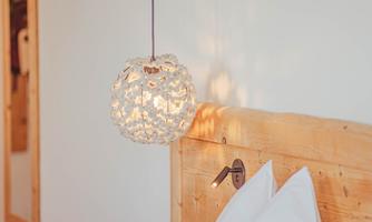 A cozy bedroom with a wooden bed frame and two white pillows. Above the bed hangs a stylish, round lamp.