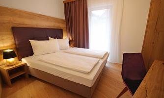 A cozy bedroom with a double bed and modern wooden decor. The room is bright and inviting, with a desk and a chair.