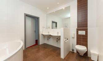 A modern bathroom with bright tiles and elegant fixtures. The amenities include a bathtub, a toilet, and double sinks.