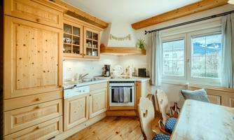 A cozy kitchen with wooden cabinets and a large table. The window offers a view of the landscape.