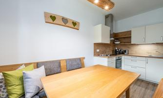 A modern kitchen with a large wooden table and a cozy seating area. The walls are painted in warm colors, and the furniture is functional and stylish.