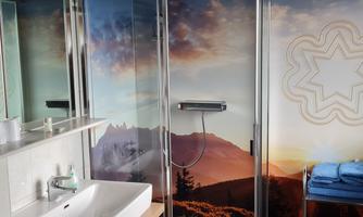 A modern bathroom with a shower cubicle and a picturesque wall decoration of mountains. On the sink, there is a soap dispenser and freshly folded towels are ready.