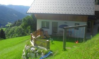 A cozy house in the mountains with a garden and a swing. In the background, green meadows and mountains can be seen.